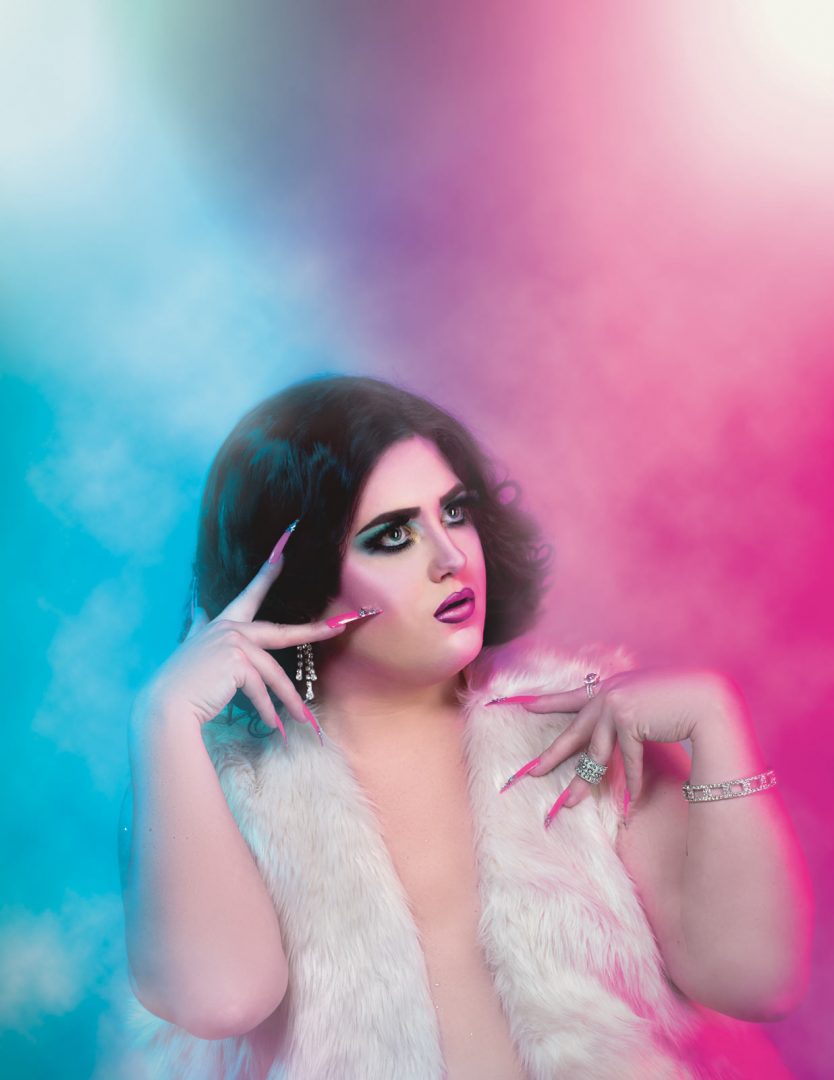 Portrait of Drag Queen and Entertainer Athena McQueen in front of Blue & Pink Fog covered backdrop with colored lighting By Brandon Marsh Photography in Guelph Ontario photo studio